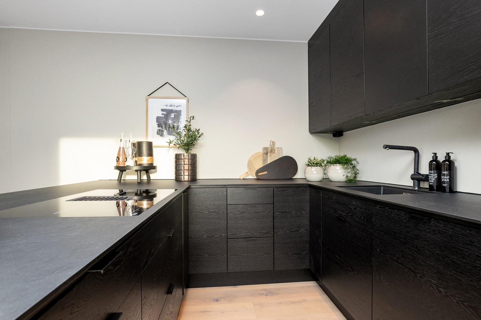 Moderne sort kjøkkeninnredning med slette skap - og skuffefronter kombinert med høytrykkslaminerte benkeplater og spiseplass. Galleribilde