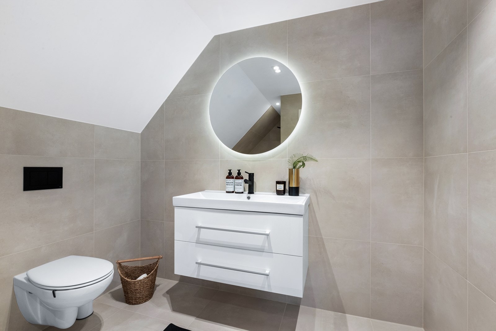 Badet er utstyrt med hvit skuffeinnredning med overliggende servant, speil på vegg med bakenforliggende belysning, vegghengt toalett og dusjnisje med nedfelt dusjsone. Galleribilde