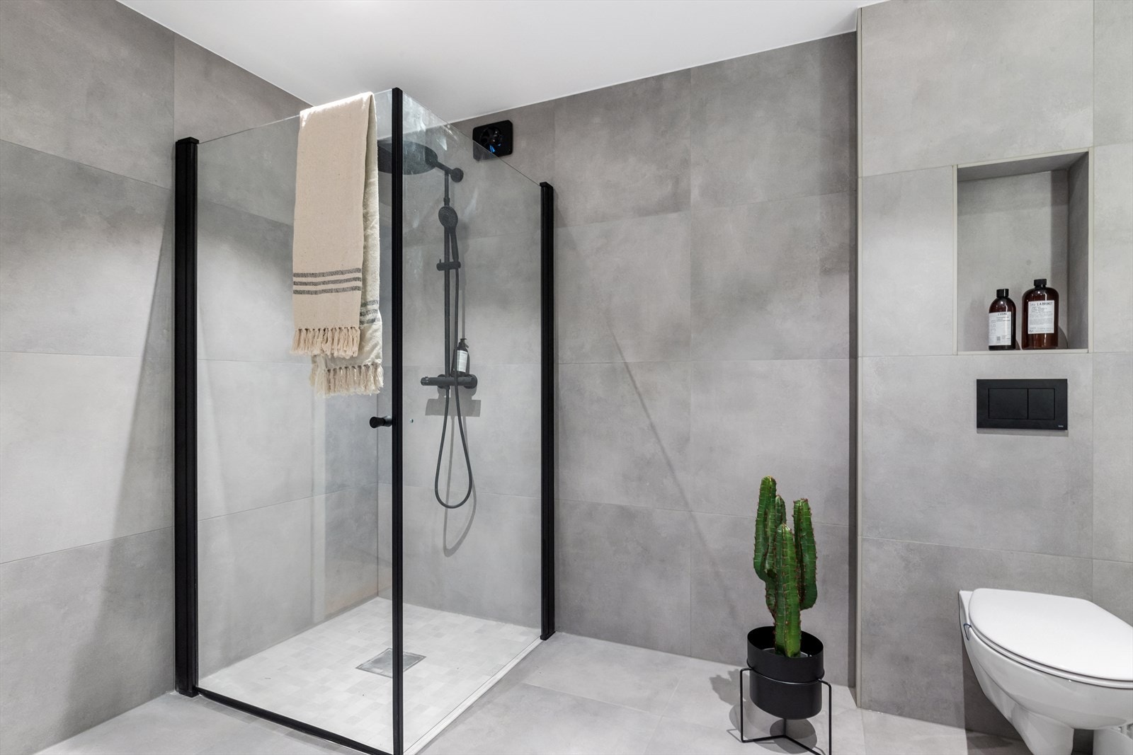 Badet er innredet med hvit skuffeinnredning med overliggende servant, vegghengt toalett med utenpåliggende sisterne med integrert hylle, dusj med nedsenket dusjsone og innfellbare glassvegger. Galleribilde