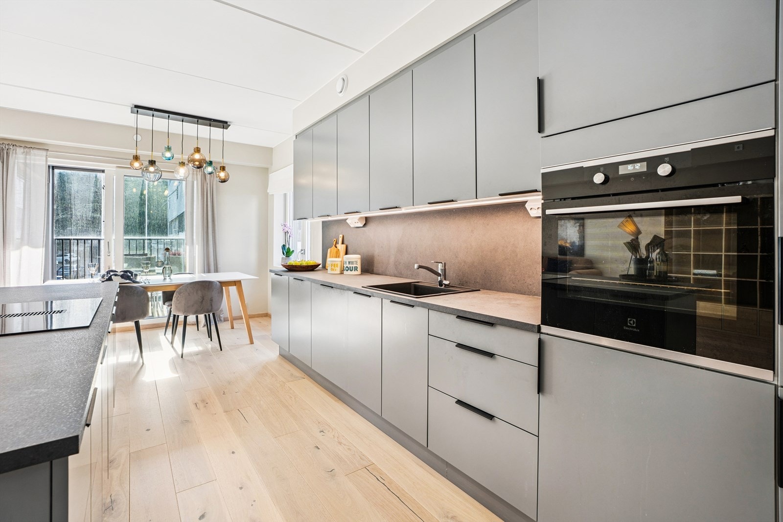 Kjøkkenet har en moderne innredning med glatte fronter, laminert benkeplate og integrerte hvitevarer som komfyr, koketopp, kjøleskap og oppvaskmaskin. Galleribilde