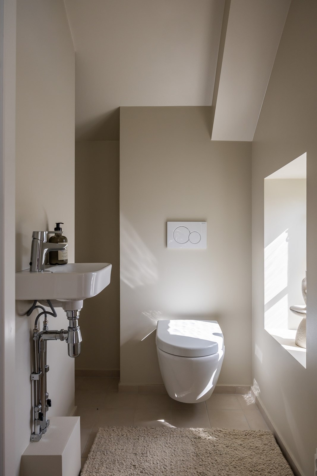 Pent toalettrom med vegghengt toalett og servant av porselen. Galleribilde