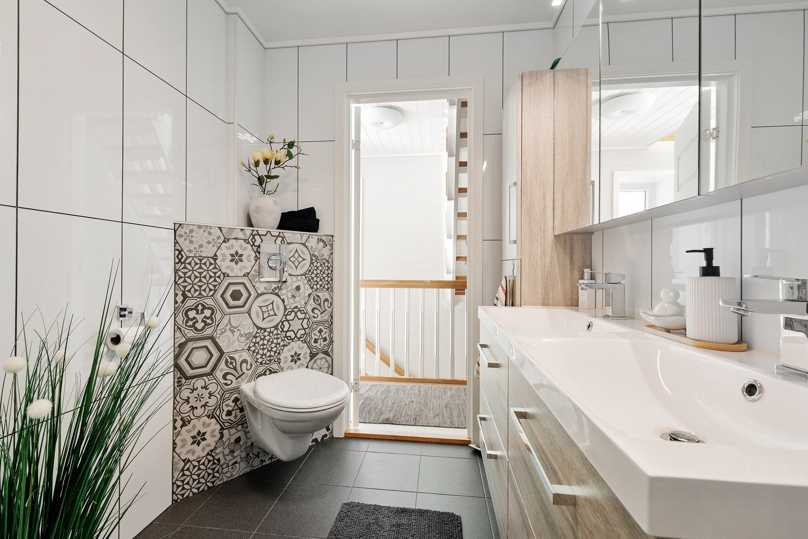 Bad har flislagt gulv med gulvvarme, flislagte vegger og malte flater i himling. Baderomsinnredning med ovenpåliggende dobbel servant med ett-greps armaturer. Speilskap med overlys over servanter. Galleribilde