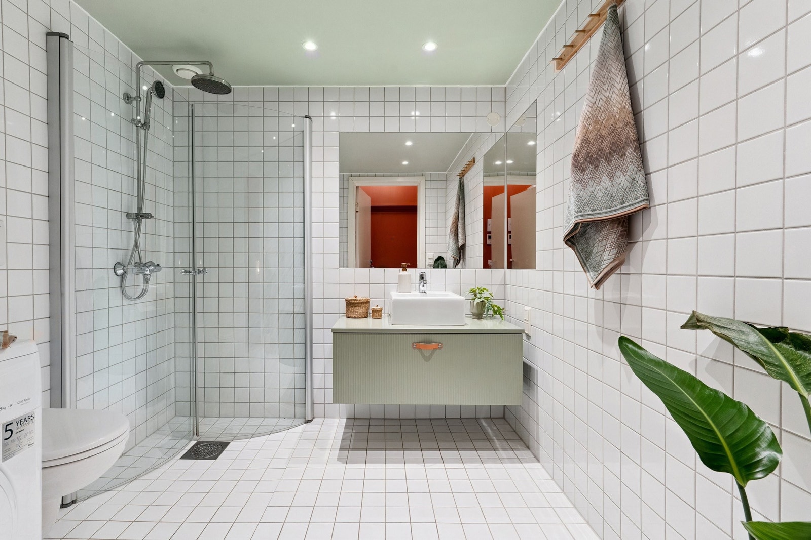 Romslig og delikat baderom med innfelte spotter, regnfallsdusj, vegghengt toalett og opplegg for vaskemaskin og tørketrommel. Galleribilde