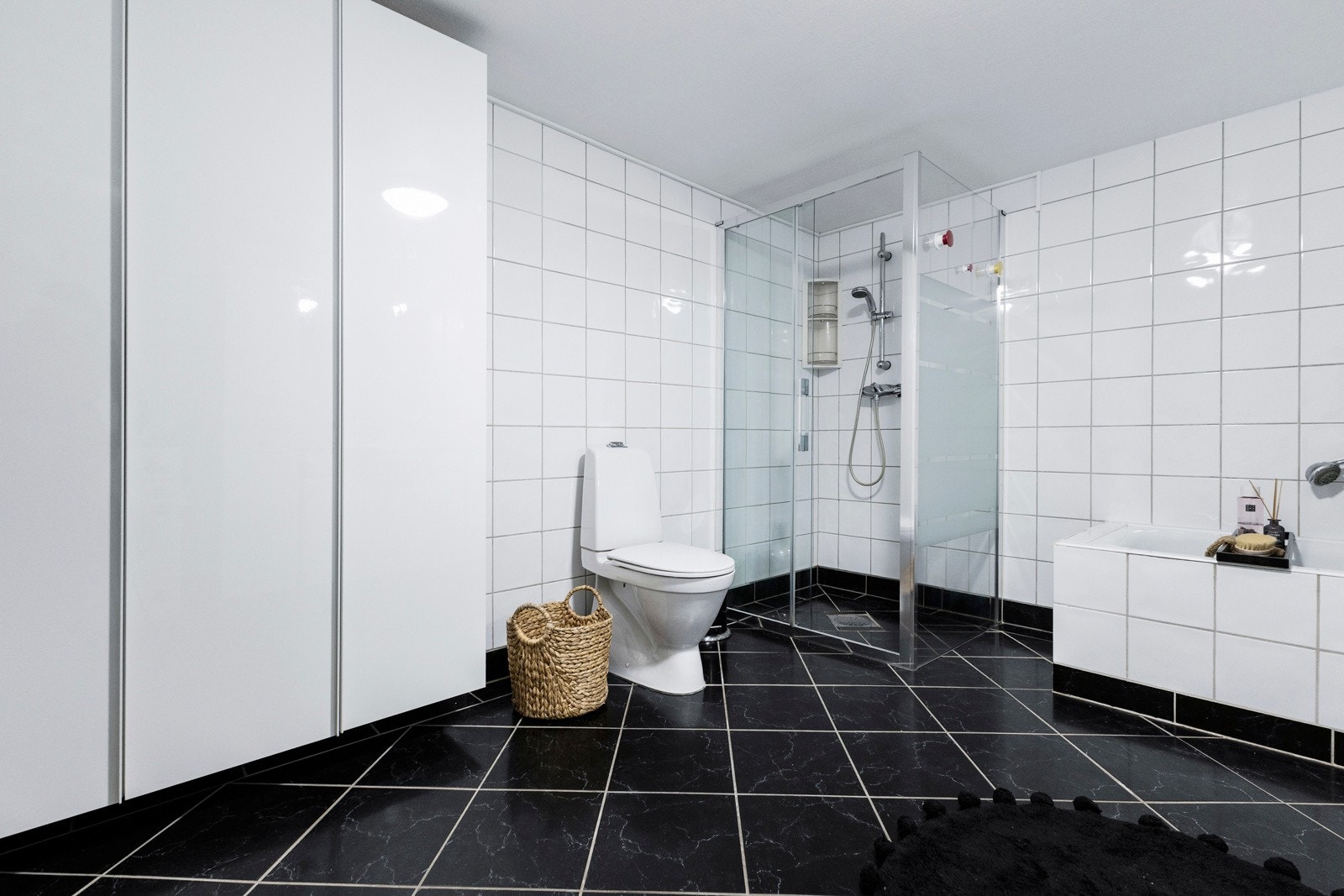 Badet er innredet med glatt baderomsinnredning med heldekkende servant nedfelt i underskap, speilskap med belysning, toalett, dusjhjørne med glassdører samt badekar. Galleribilde