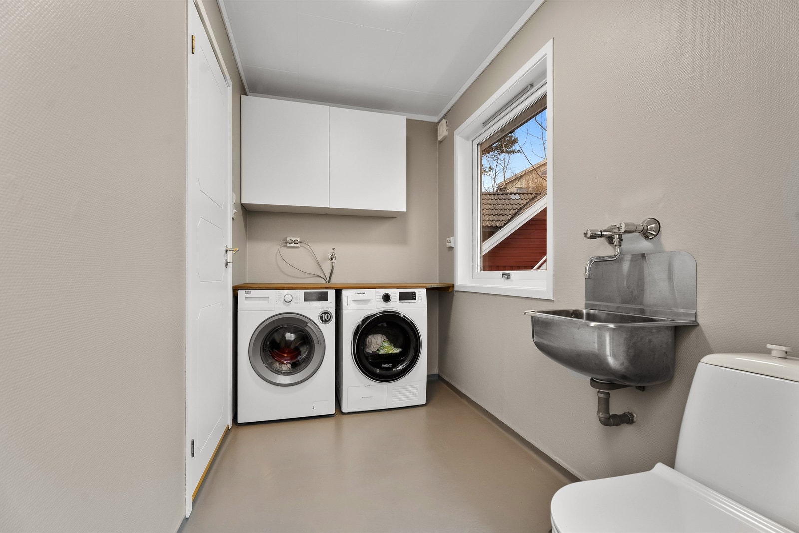 Fra kjøkkenet er det inngang til et praktisk vaskerom med plass til vaskemaskin og tørketrommel. Det er utslagsvask, praktisk arbeidsbenk, toalett og overskap. Egen utgang til siden av huset. Galleribilde