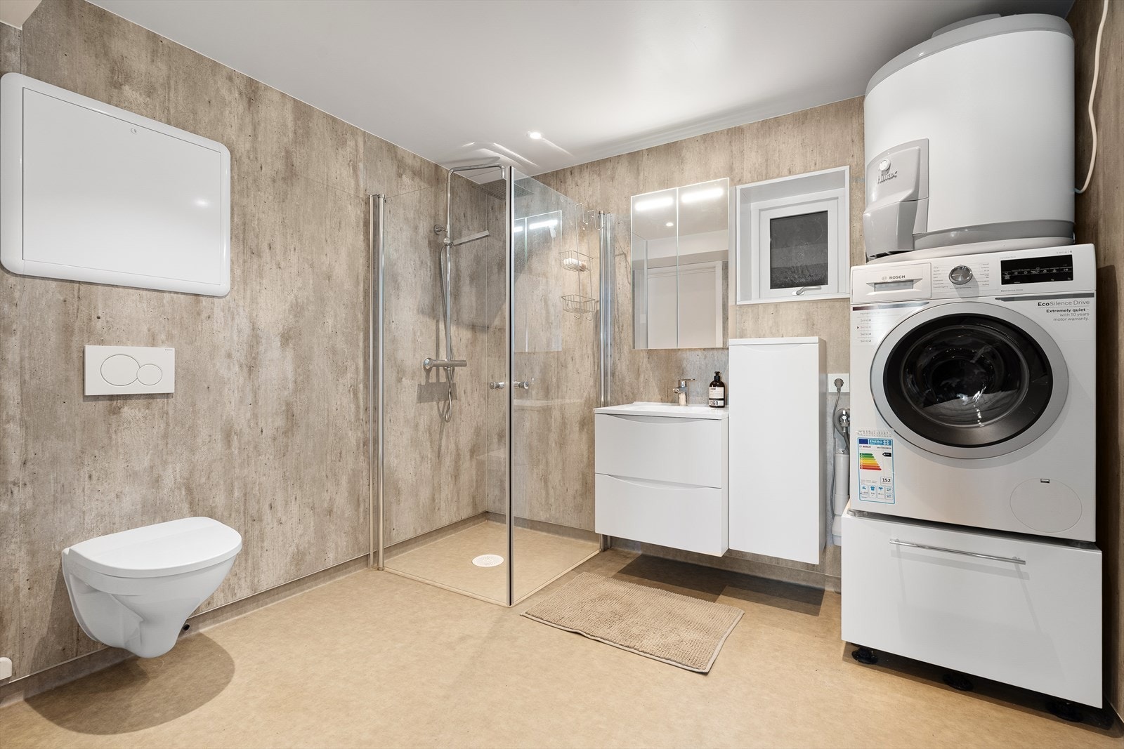 Stort bad med vegghengt toalett, servant med innredning og dusjhjørne. Opplegg til vaskemaskin. Galleribilde