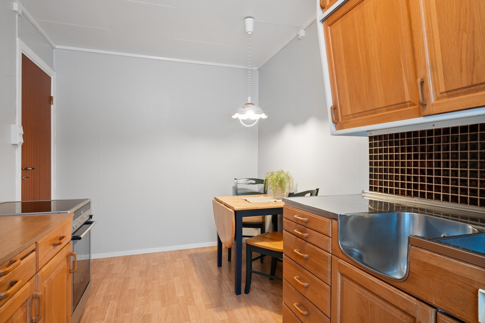 Kjøkkeninnredning i tre med heldekkende benkebeslag i stål. Galleribilde