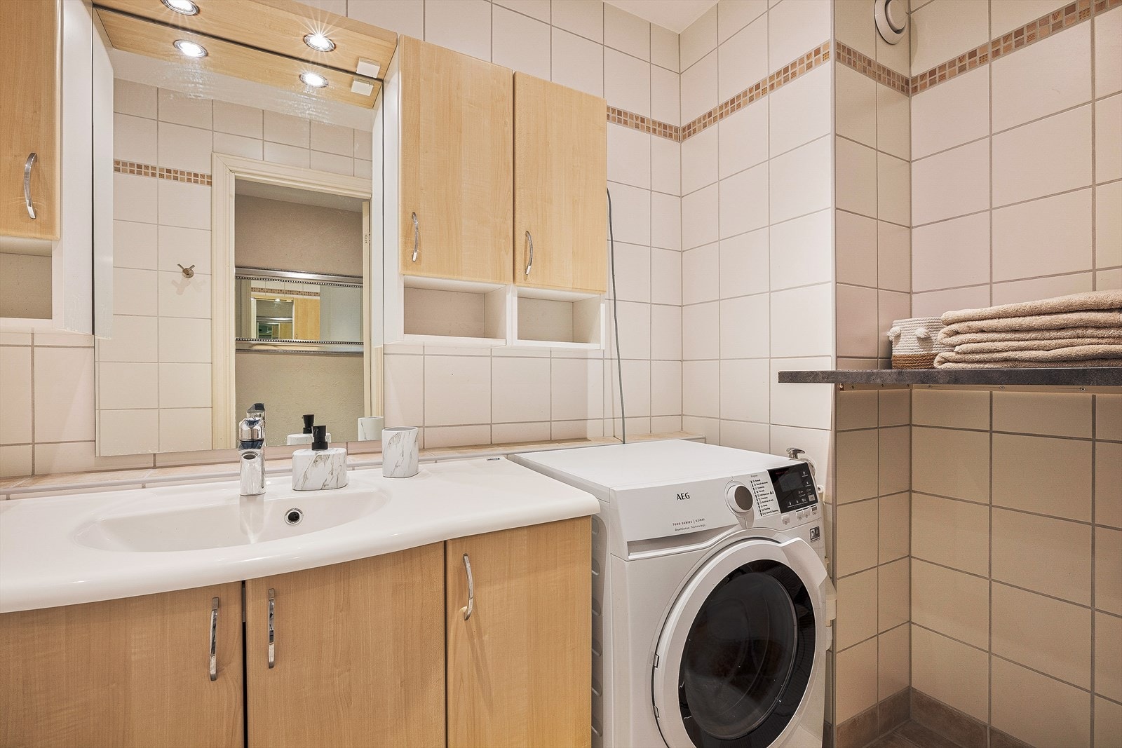 Badet har innfliset badekar med dusj, opplegg for vaskemaskin samt vask med møblement, speil og belysning Galleribilde