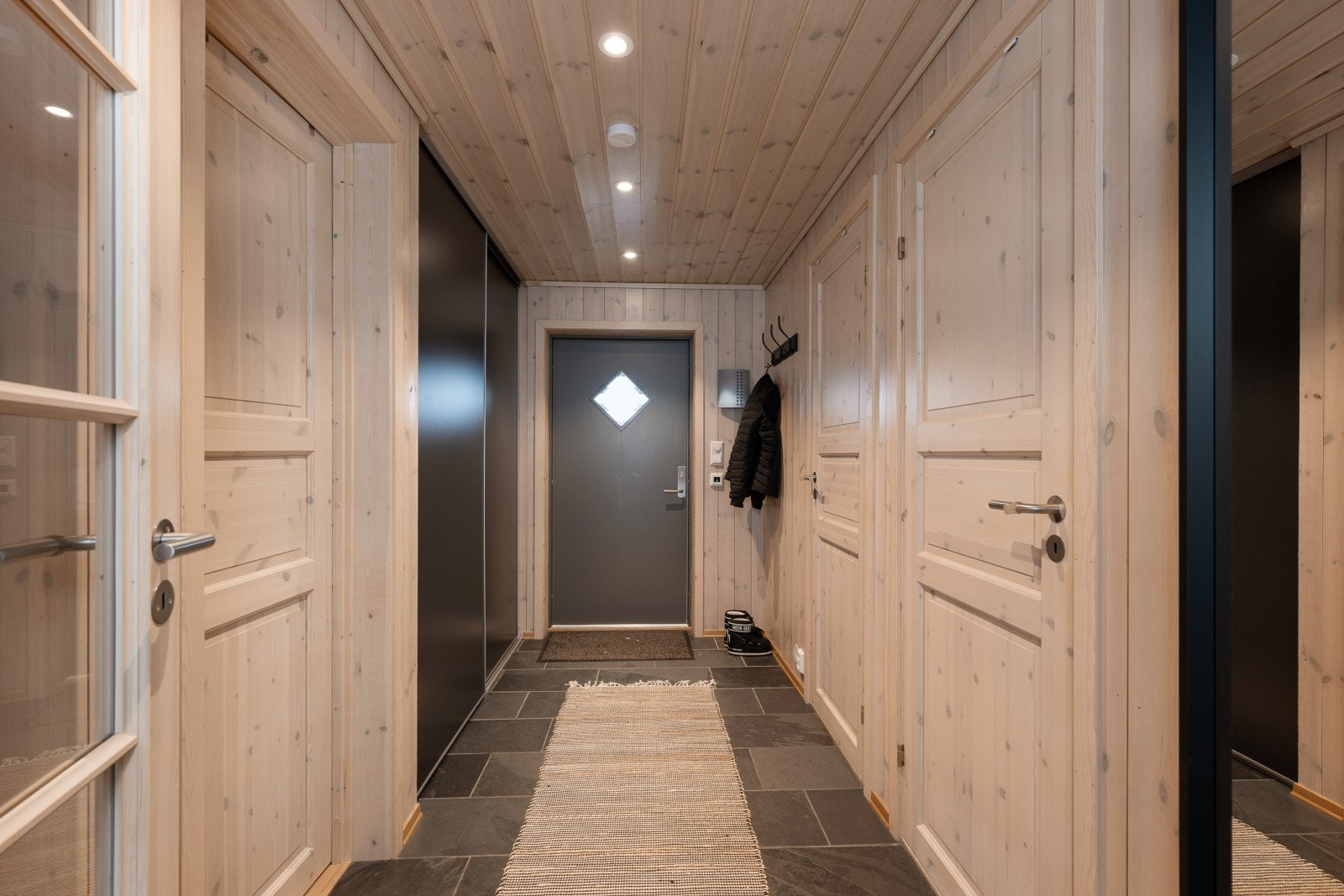 Entréen gir en fin smakebit av leilighetens standard. Panel på overflater skaper en lun atmosfære og den rette hyttefølelsen. Det er montert en praktisk skyvedørsgarderobe i entréen. Galleribilde