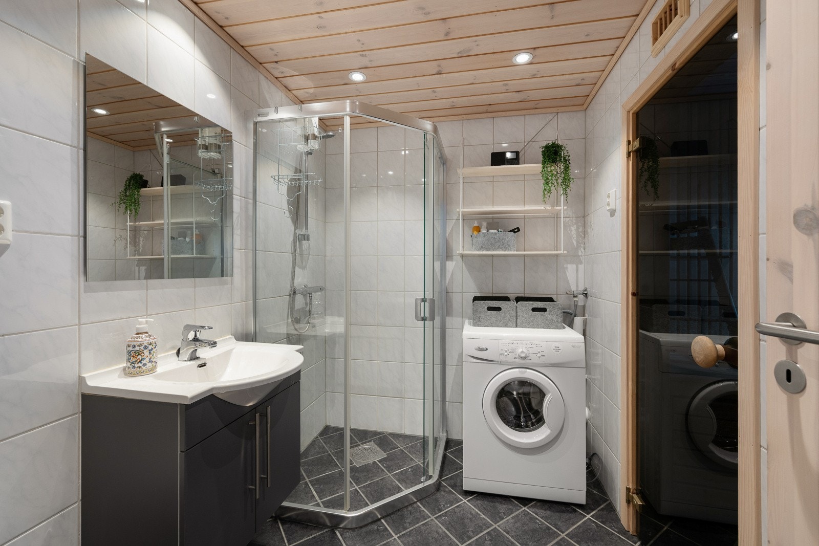 Pent bad med flislagte overflater og varmekabler i gulvet. Badet innehar servantinnredning, speil, dusjhjørne, vegghengt toalett og opplegg for vaskemaskin. Galleribilde