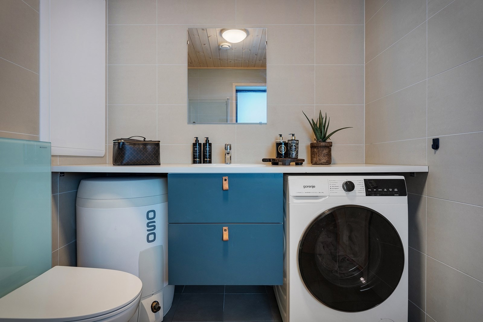 Badet er utstyrt med foldedører i dusjen, veggtoalett, opplegg for vaskemaskin og baderomsinnredning med servant, samt belyst speil Galleribilde