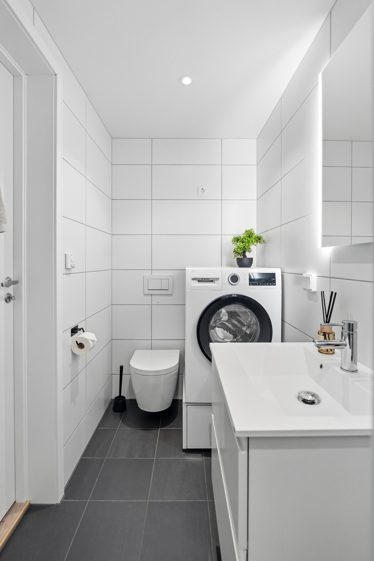 Videre er badet utstyrt med vegghengt toalett, servant i innredning med speil og integrert belysning Galleribilde