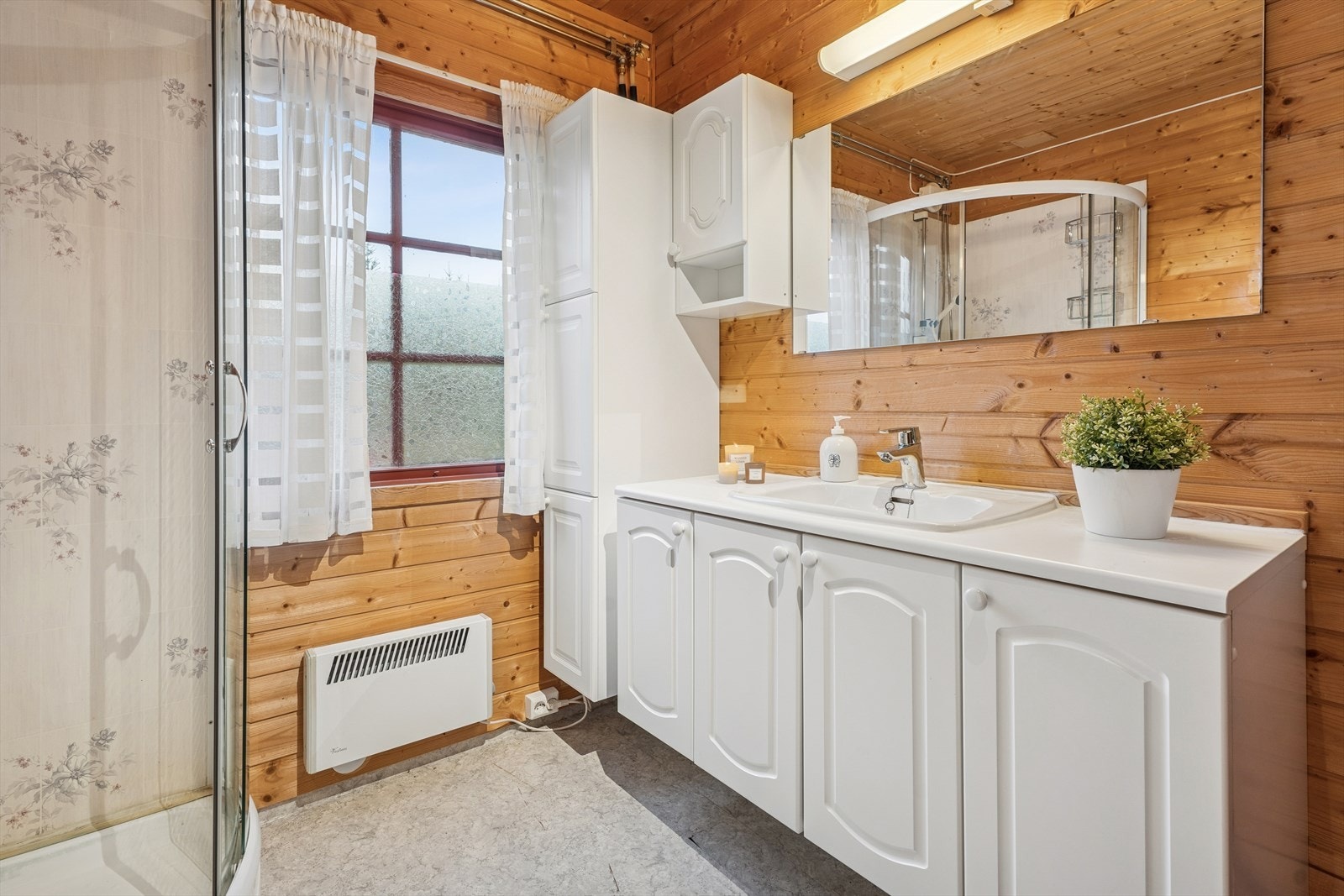 Badet er praktisk innredet med servantskap, tilhørende høyskap, dusjkabinett og et gulvmontert toalett som var nytt i 2025. Galleribilde