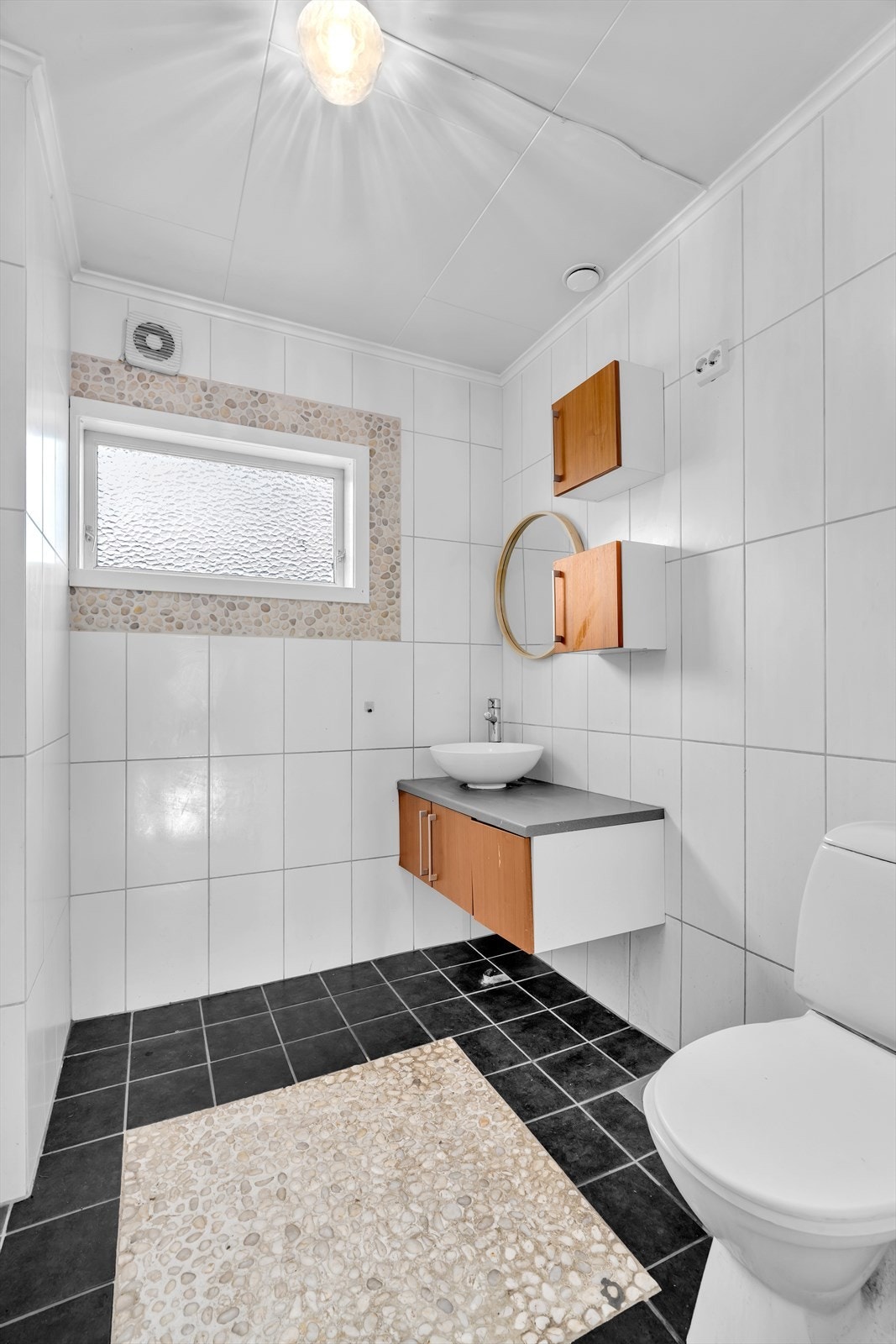 Badet i 1. etasje ble oppgradert i 2016 og har et moderne og stilrent uttrykk med fliser på både gulv og vegger. Det er utstyrt med en praktisk innredning som inkluderer vask og WC. Galleribilde