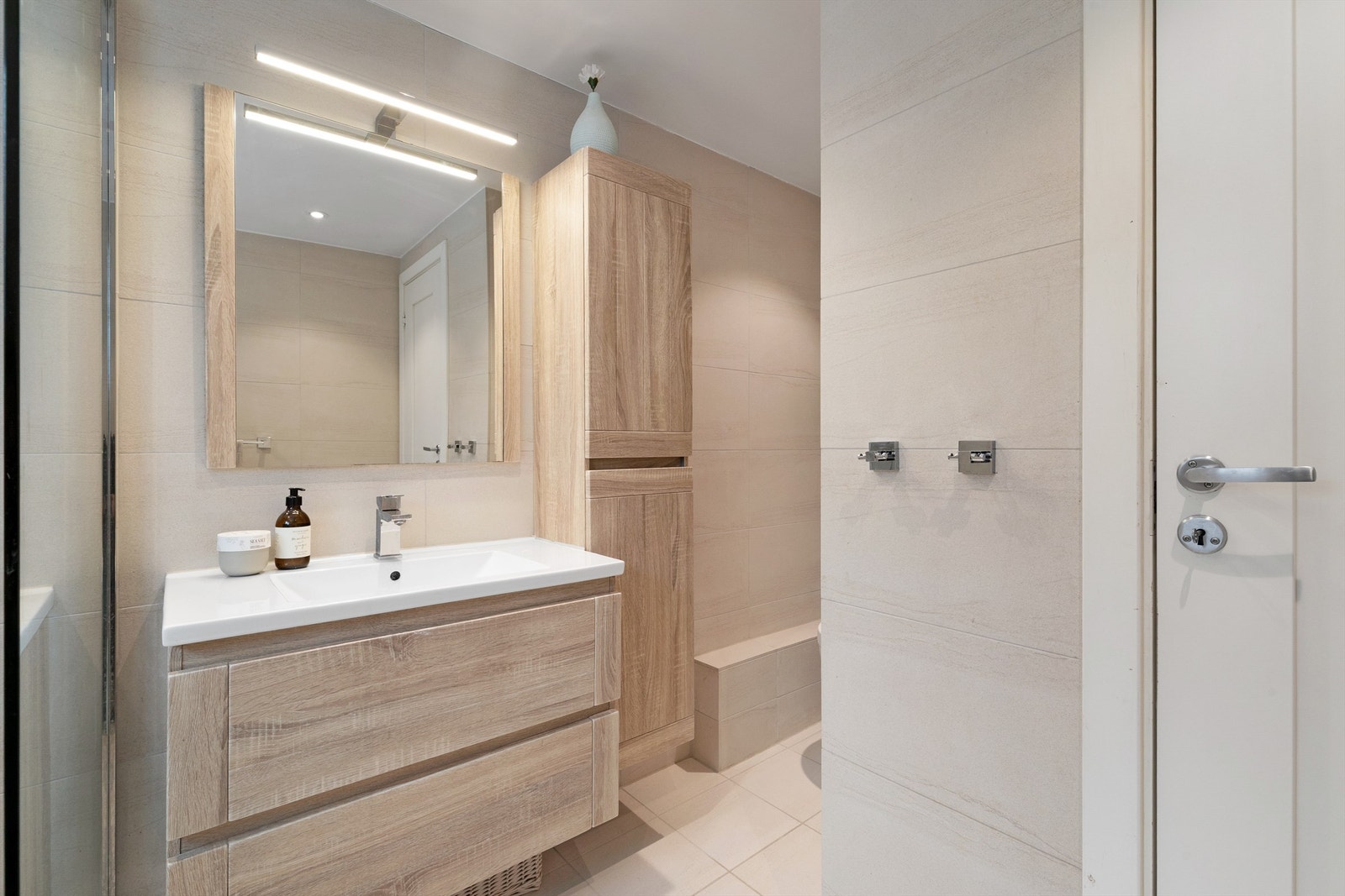 Baderomsmøblene har fronter i lys trestruktur, som står svært godt til de beige flisene. Godt med ekstra lagringsplass i høyskap Galleribilde