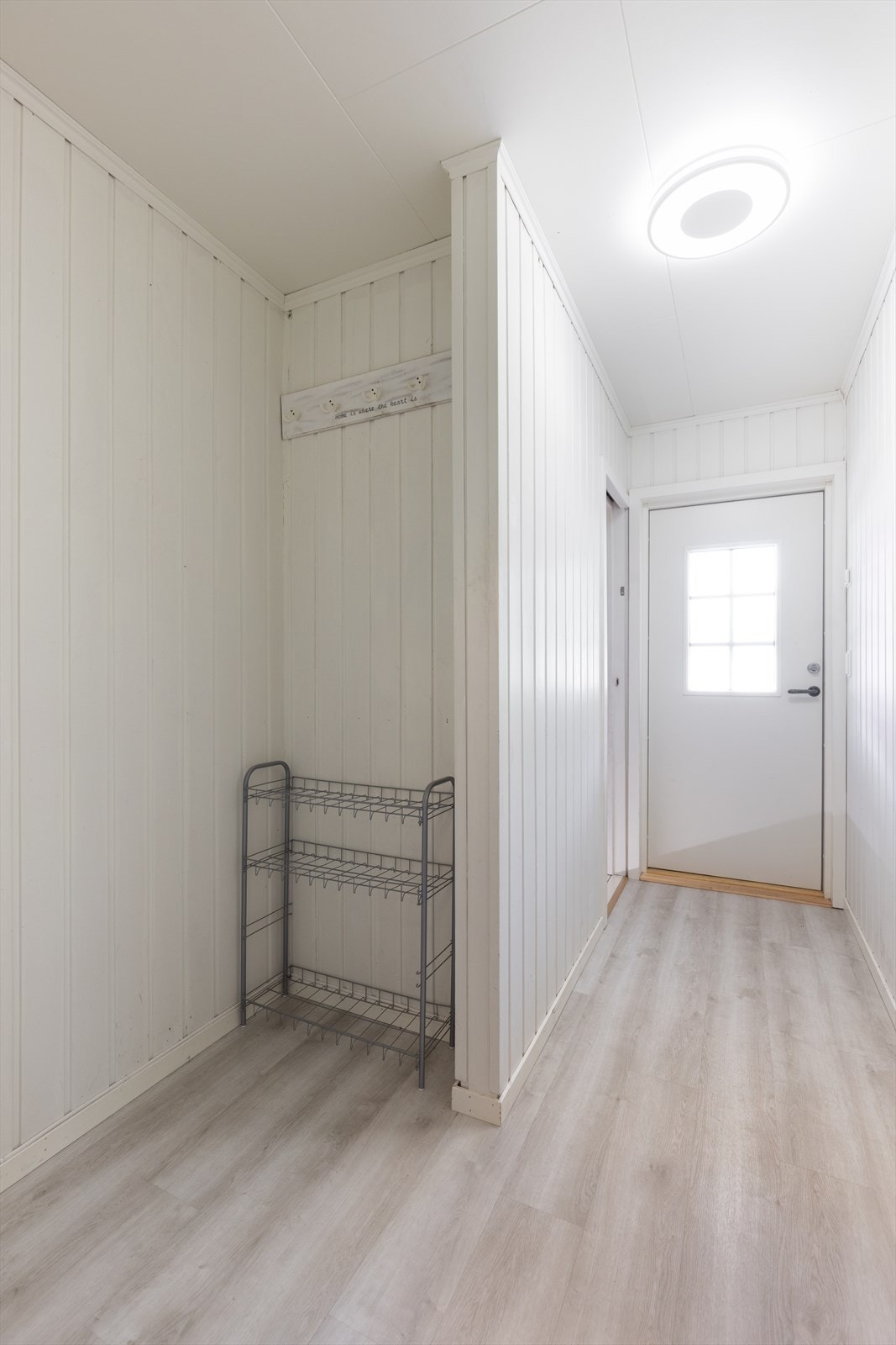 Med adkomst fra koselig, overbygget inngangsparti kommer man inn i boligens gangareal, med moderne laminat på gulvet som går videre inn i stua og kjøkkenet. Her er det en praktisk nisje til oppbevaring av sko- og ytterklær. Galleribilde