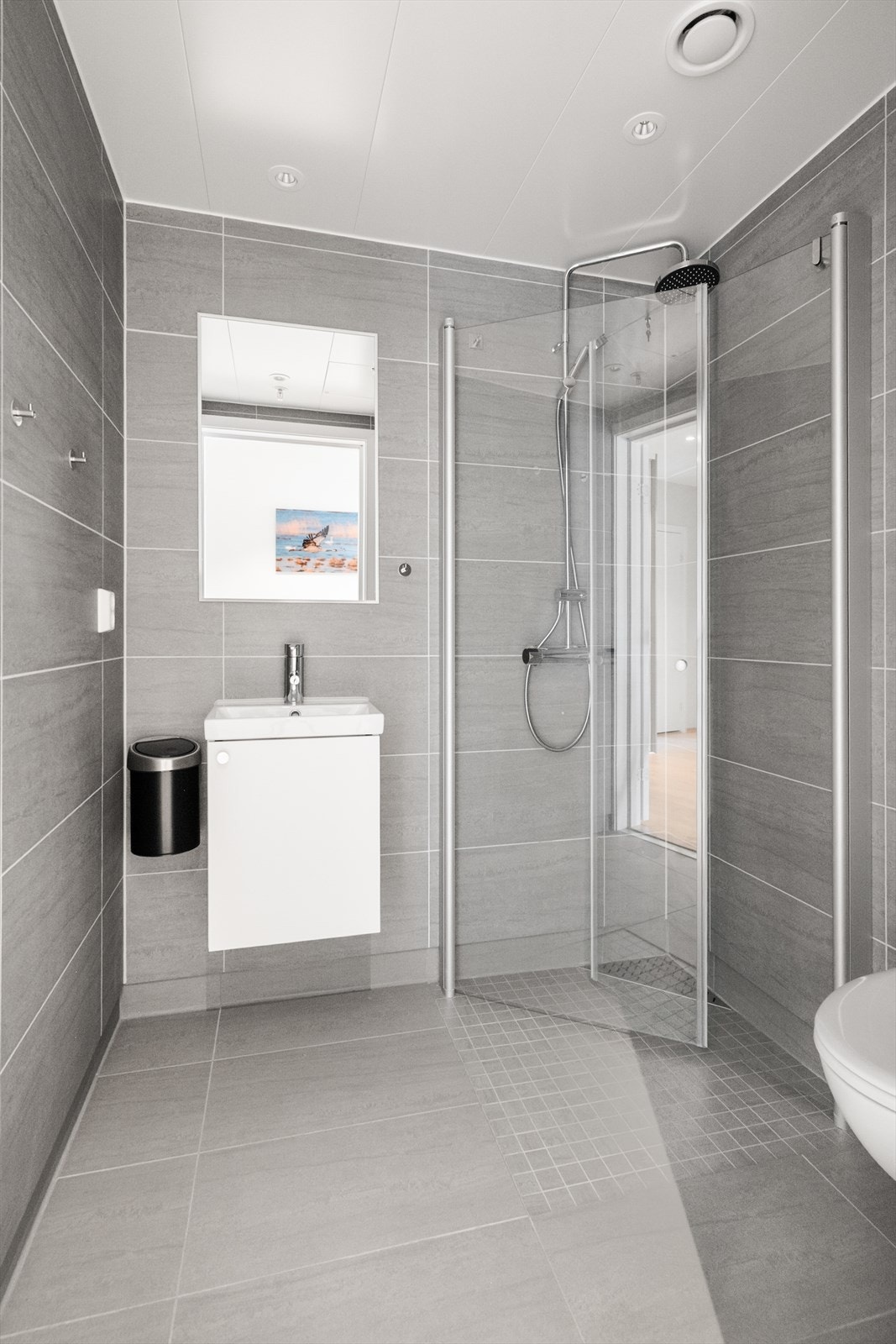 Bad nr 2 er innredet med veggmontert toalett, dusjhjørne og servantinnredning skap og speil. Det er avtrekk i tak via balansert ventilasjon. Badet har adkomst fra gangen. Galleribilde