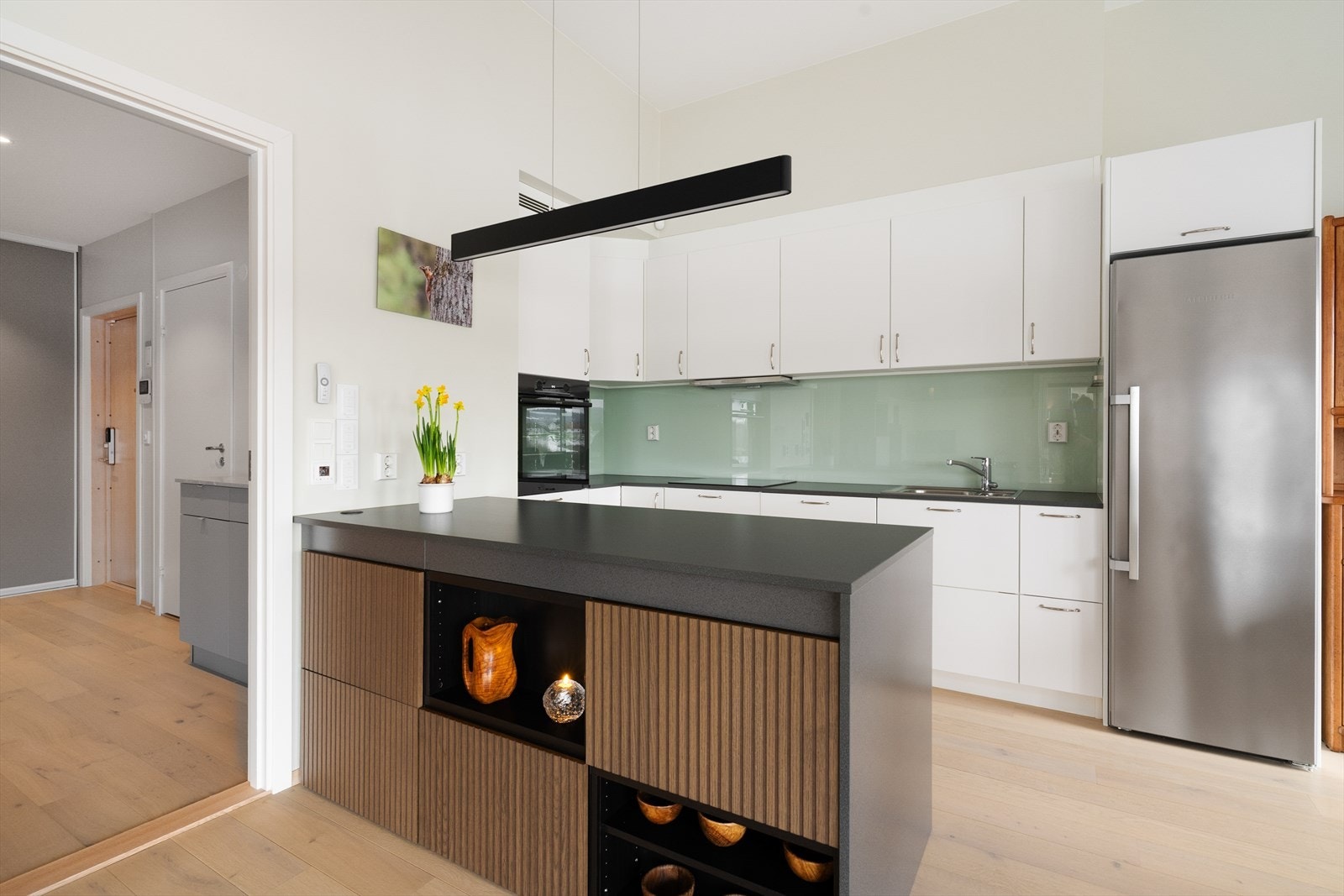 Kjøkkenet har innredning med glatte fronter og benkeplate av laminat. Praktisk øy som er utvidet på den ene siden med samme skapinnredning som i stuen, noe som gir en fin helhet i rommet. Galleribilde