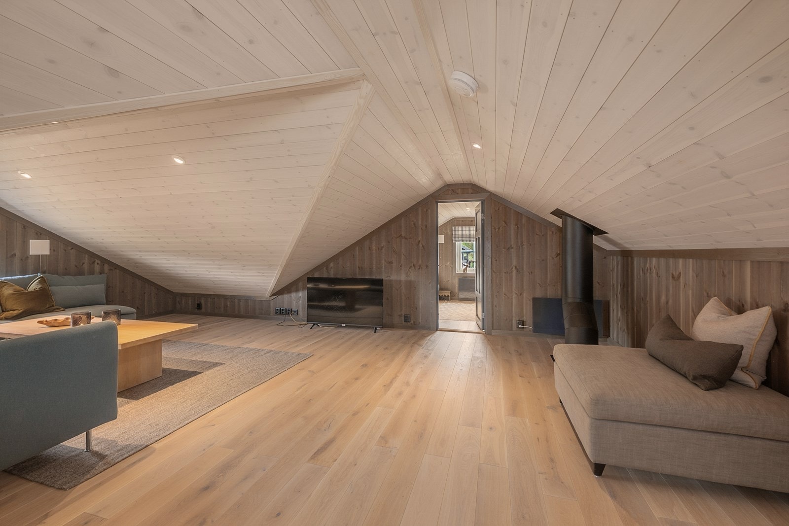 En utrolig stor og praktisk hems er delt inn i brukervennlig stue og 2 rom innredet med senger. Lys panel i tak og og lune vegger i fin kombinasjon med 1-stavs parkett i eik. Galleribilde