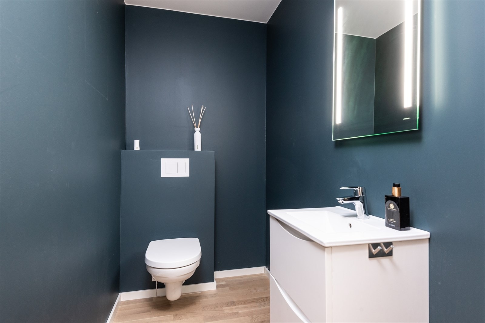 Vegghengt toalett med innebygget sisterne gir et stilrent uttrykk. Parkettgulv og mørke vegger skaper et moderne innemiljø på toalettrommet. Galleribilde