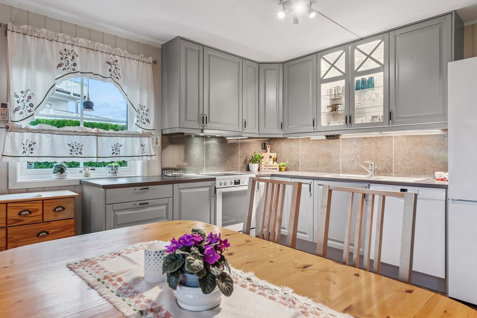 Klassisk innredning med fronter i en pen og lys gråfarge. Plass for frittstående hvitevarer. Oppvaskmaskin medfølger. Galleribilde