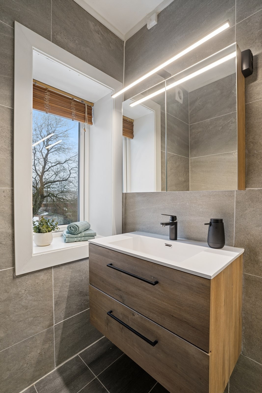 Her finner du en praktisk innredning med nedfelt servantmed underskap, speilskap med god belysning, samt vegghengt toalett som gir et rent og ryddig uttrykk. Galleribilde