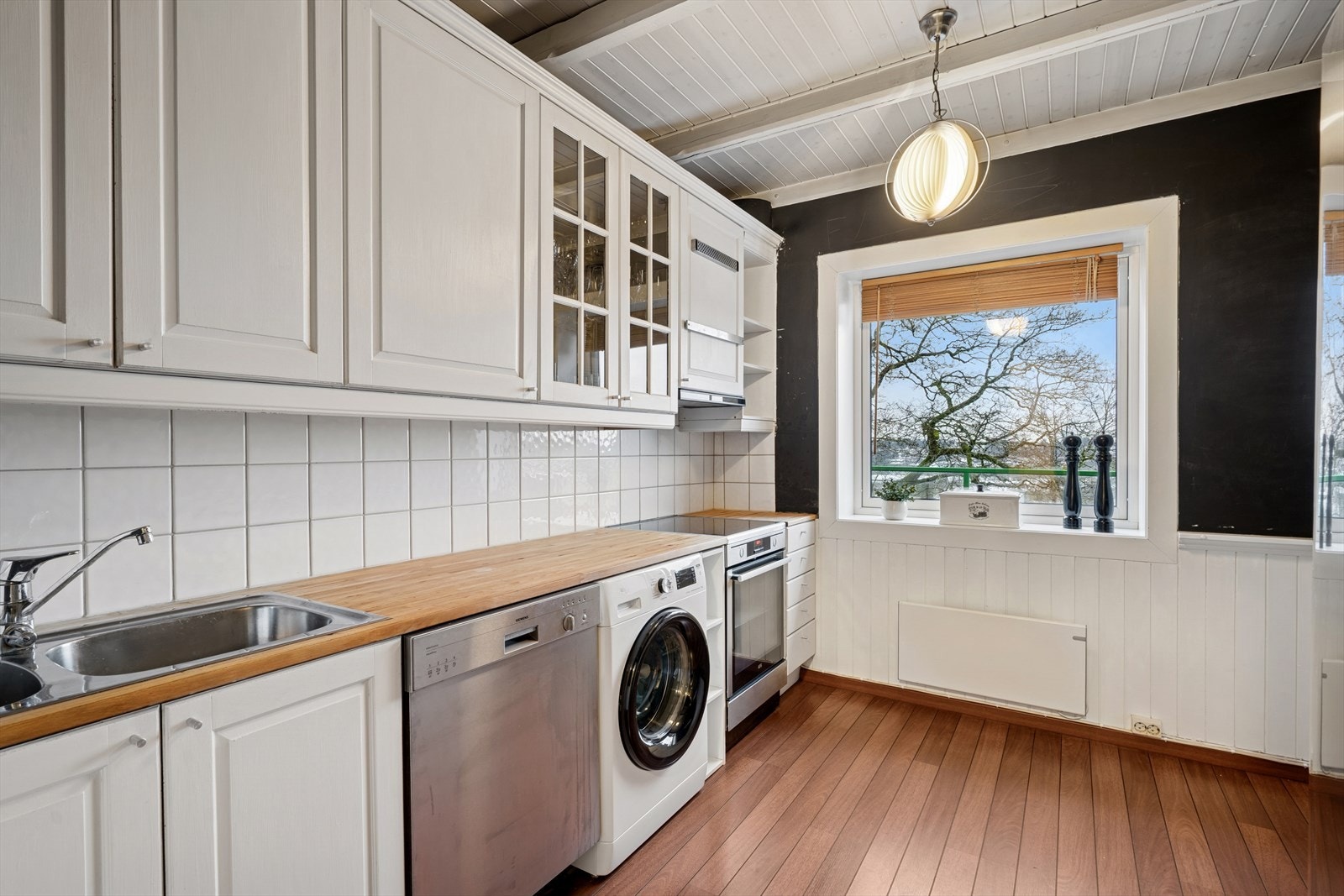 Kjøkkenet er fra IKEA og er innredet med hvite profilerte fronter kombinert med heltre benkeplate og fliser over benk. Galleribilde