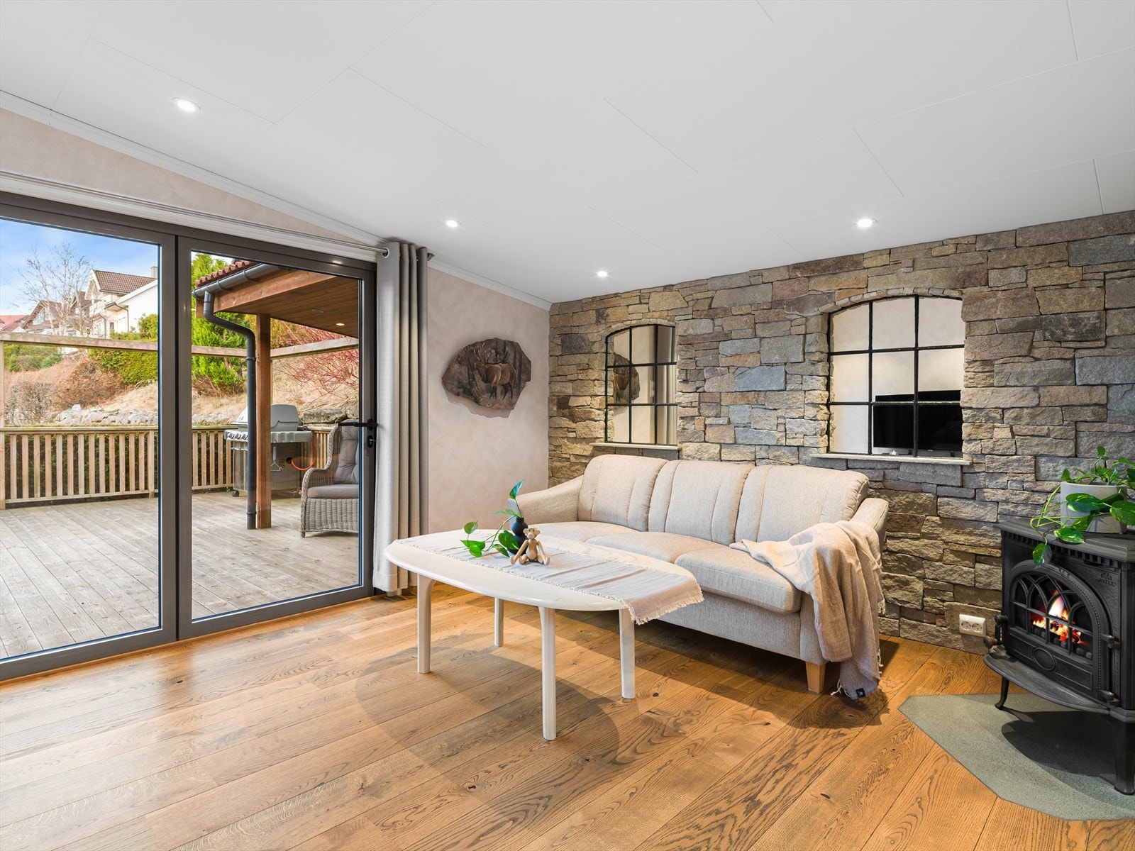 Tv-stua har flott stenlødd vegg og vedovn. Utgang både til baksiden av huset og til stor og solrik terrasse. Galleribilde