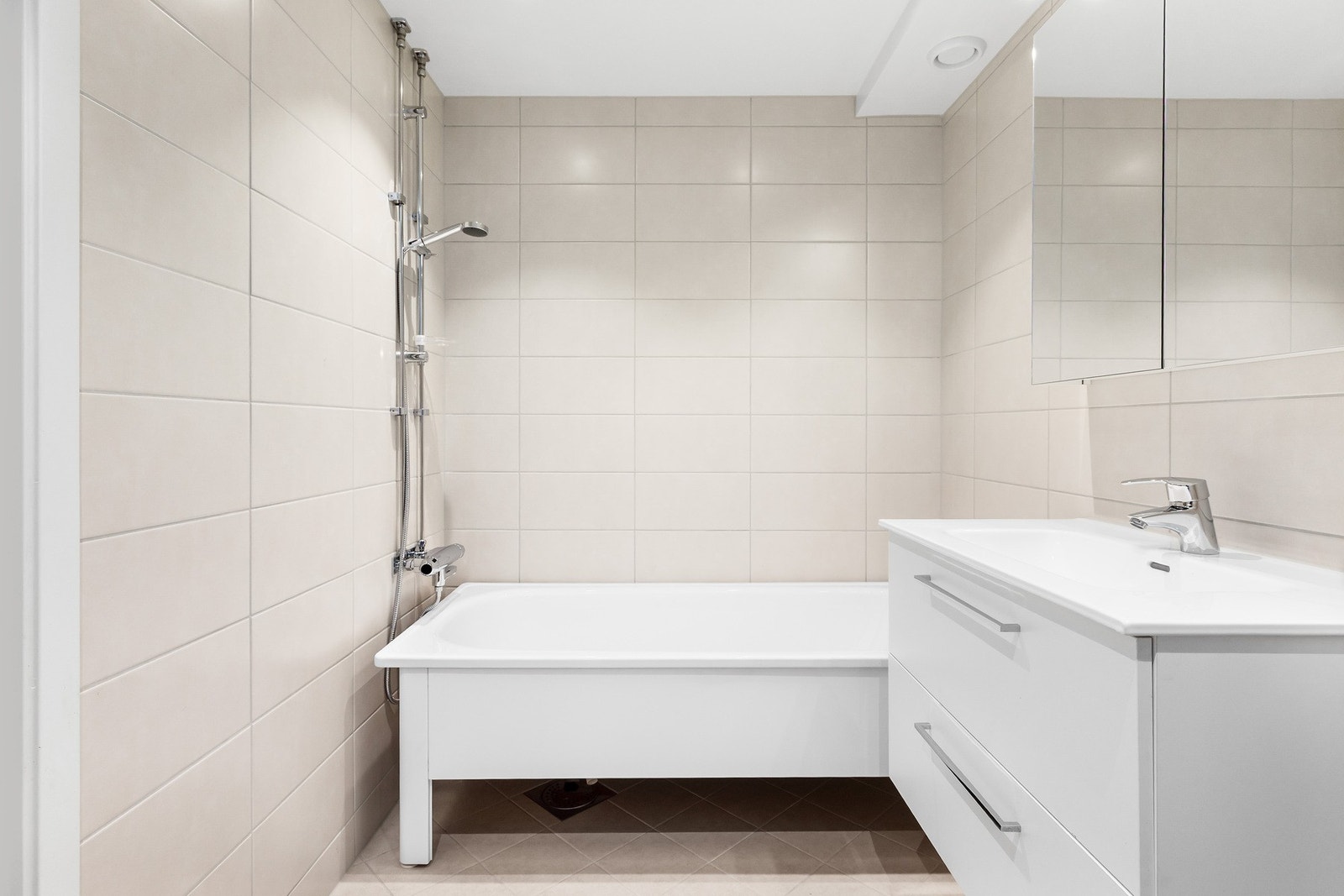 Badet er innredet med vegghengt toalett, servantskap, speilskap med overbelysning og badekar Galleribilde