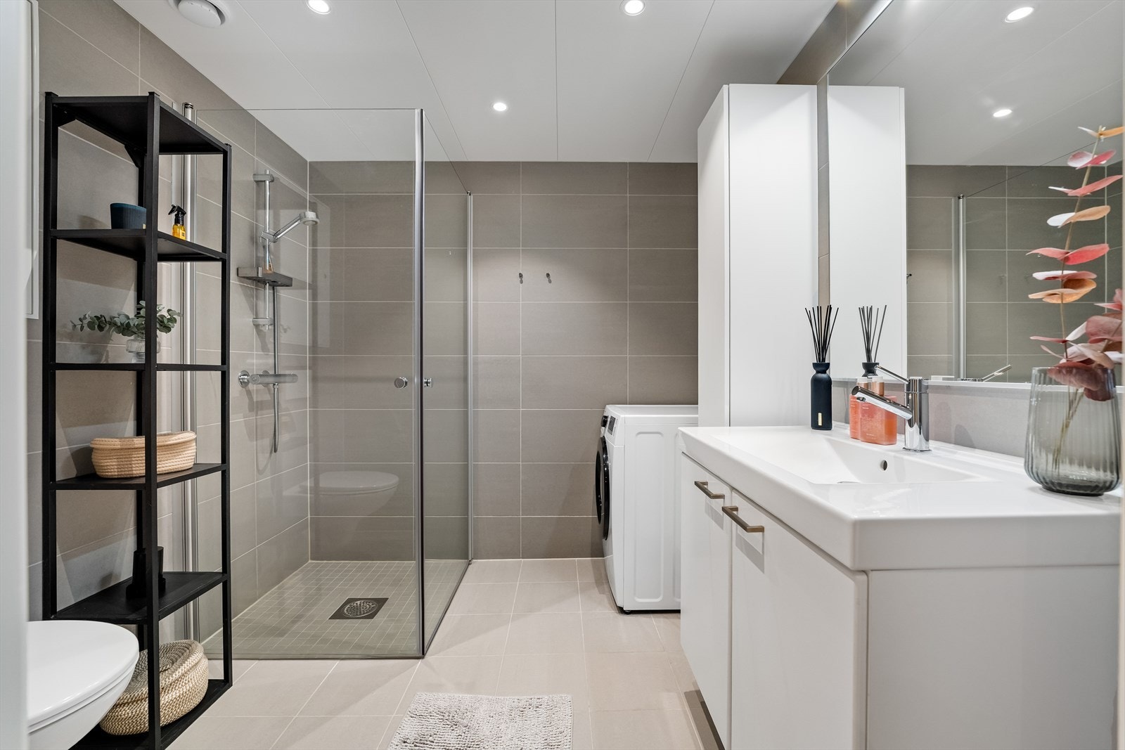 Lekkert flislagt bad med moderne innredning, dusjhjørne med glassdører og opplegg for vaskemaskin. Galleribilde