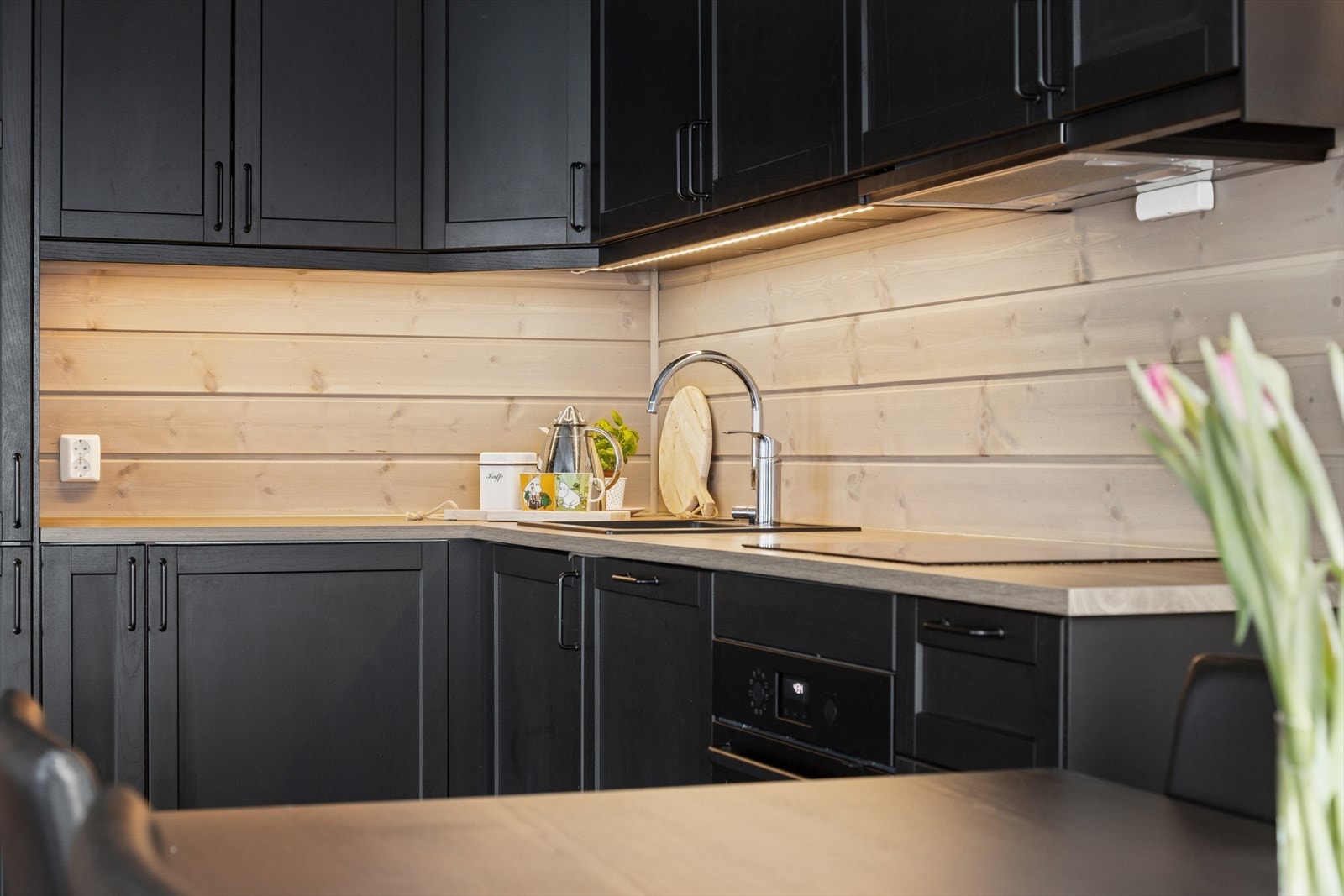 Her er det en stilfull kjøkkeninnredning utført med sorte, profilerte fronter, benkeplate i laminat og kjøkkenkum. Galleribilde