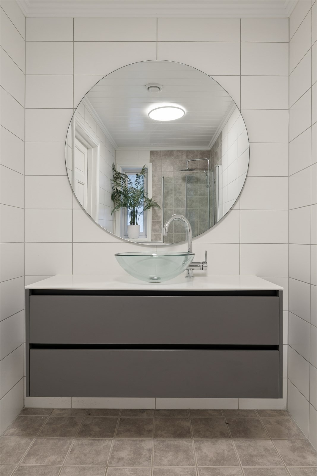 Dette badet er innredet med baderomsinnredning med benkeplate og bolleservant, speil, vegghengt toalett og dusjhjørne med dusjvegger. Galleribilde