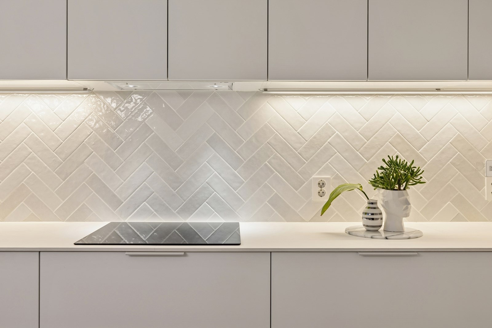 Hvit benkeplate og fliser gir et stilrent uttrykk på kjøkkenet. Galleribilde