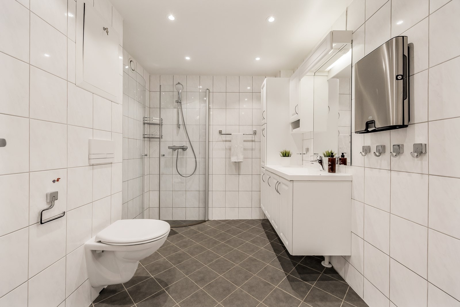 Badet er helfliset med hvite veggfliser og mørkere, diagonallagte gulvfliser. Galleribilde