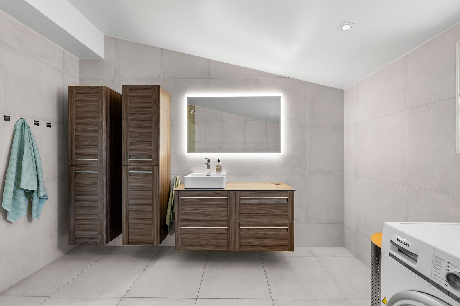 Badet er innredet med nedfelt servant, veggmontert toalett, dusjhjørne. Det er også opplegg for full vaskesøyle med vaskemaskin og tørketrommel. Galleribilde