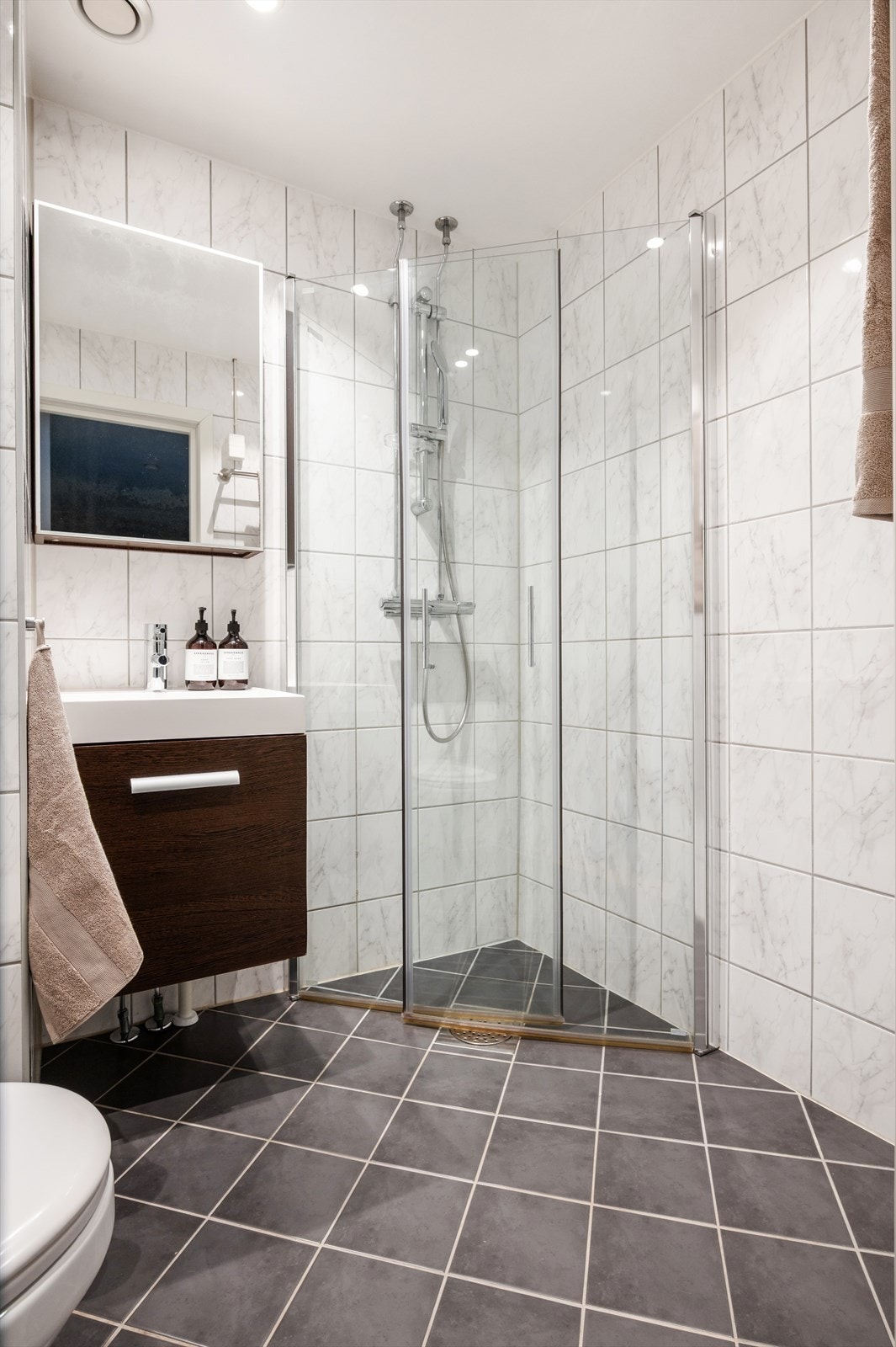 Badet er utstyrt med servant på vegghengt servantskap, samt speilskap på vegg over servant. Det er opplegg for vaskemaskin, veggmontert toalett med innebygd sisterne kasse og dusjhjørne dusjdører i glass. Galleribilde