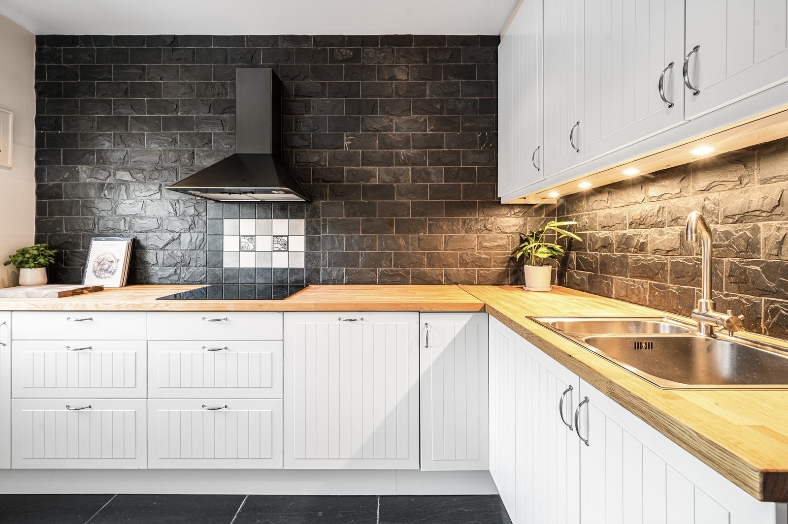 Innredning med profilerte fronter, heltre benkeplate, integrert kjøkkenkum og platetopp. Flislagt vegg over kjøkkenbenk. Galleribilde