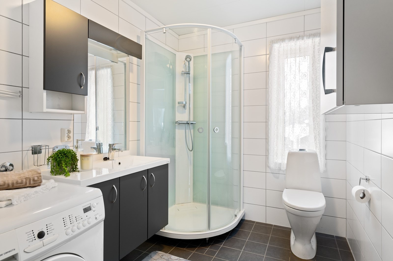 Helfliset bad med dusjkabinett, gulvmontert wc, innredning med heltrukket servant og opplegg for vaskemaskin. Galleribilde