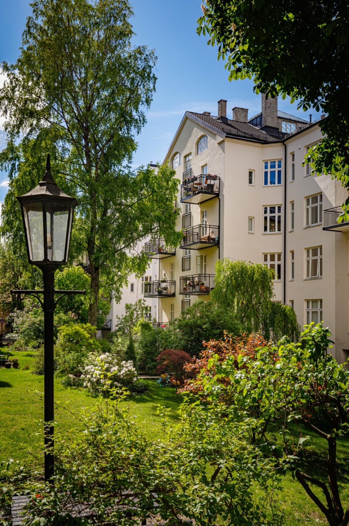 Stor felles bakhage, med gressplen, trær, sittegruppe, lekeplass og hellelagte gangarealer Galleribilde