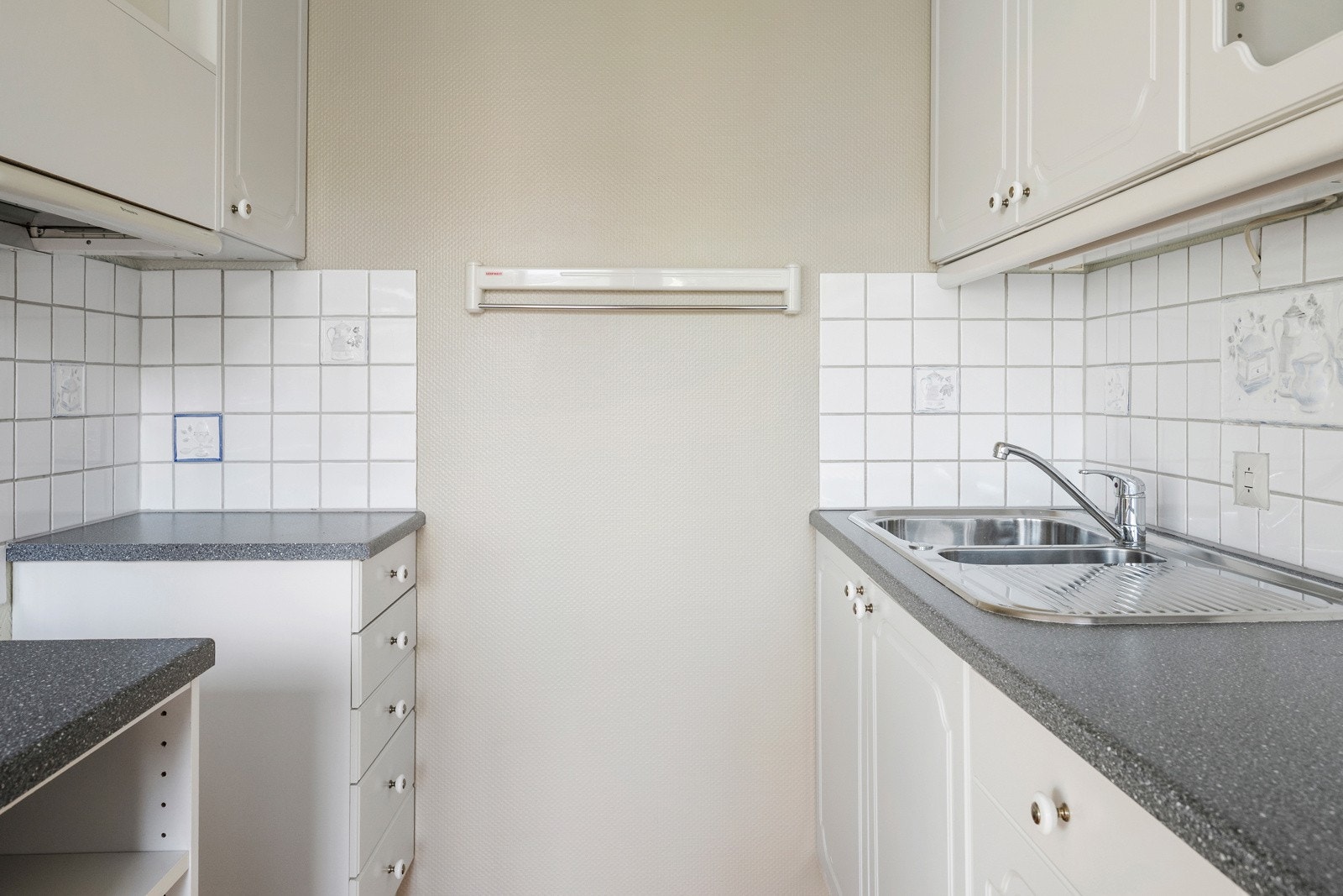 Det er lyse, profilerte fronter, laminat benkeplate med dobbel kum og fliser på veggen. Galleribilde