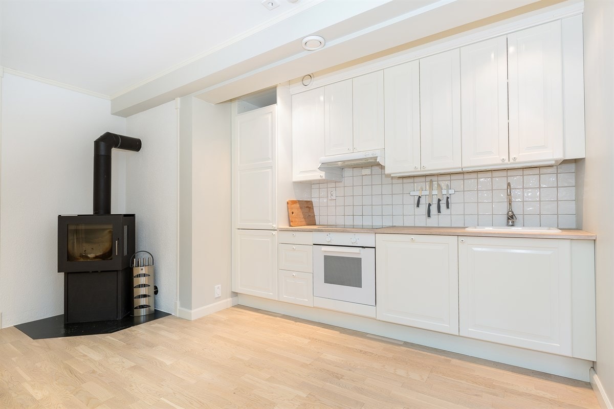 Kjøkkeninnredning med lyse profilerte fronter og eik benkeplate med oppvaskkum i porselen. Det er hvitevarer som koketopp, stekeovn, oppvaskmaskin og kjøl/fryseskap. Galleribilde