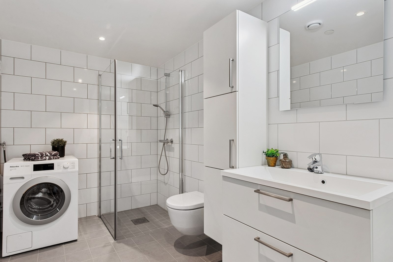 Romslig, flislagt bad med gulvvarme, dusjvegger, vegghengt toalett og opplegg for vaskemaskin. Galleribilde