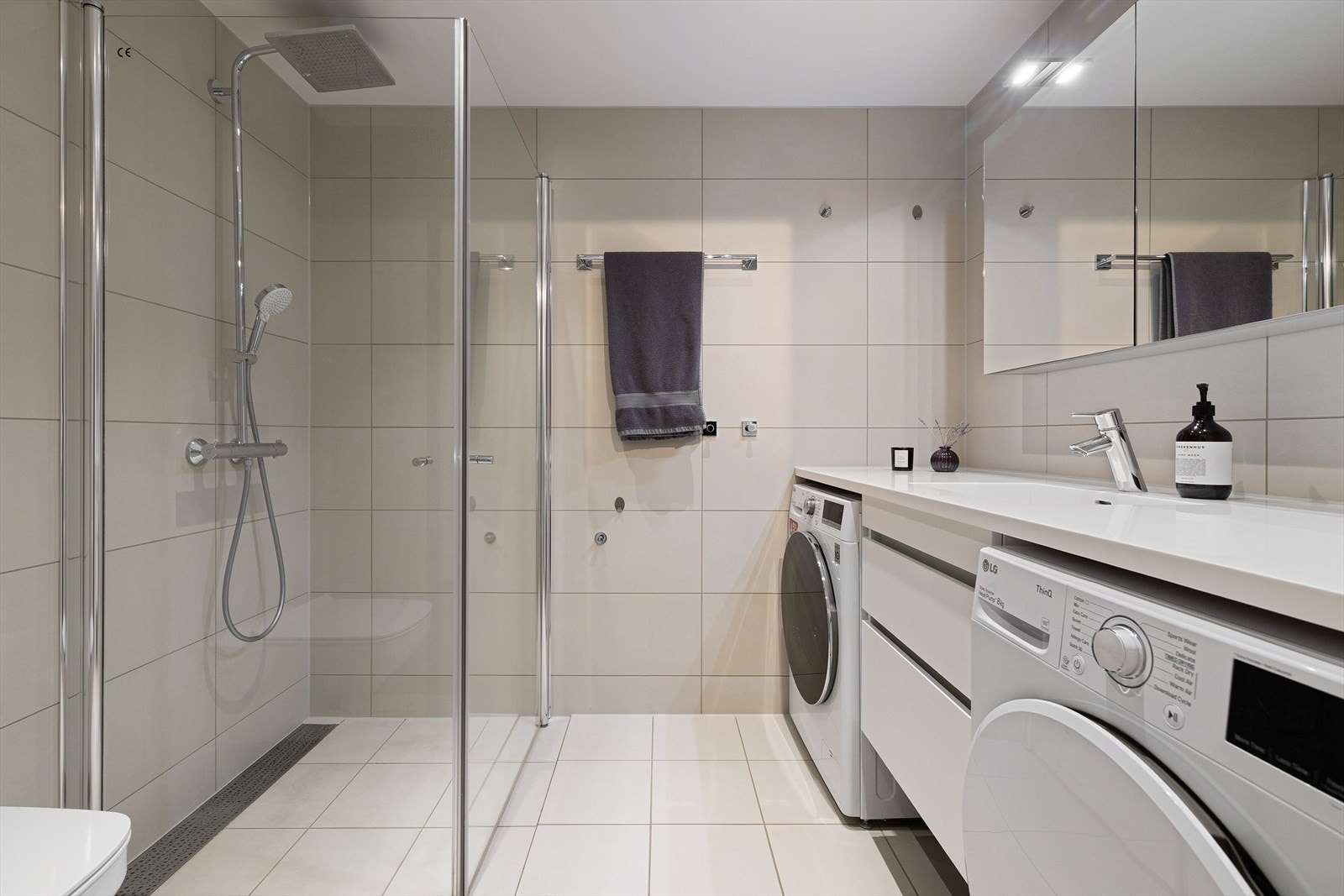 Lekkert flislagt baderom med varmekabler i gulv og opplegg for vaske og tørkemaskin Galleribilde