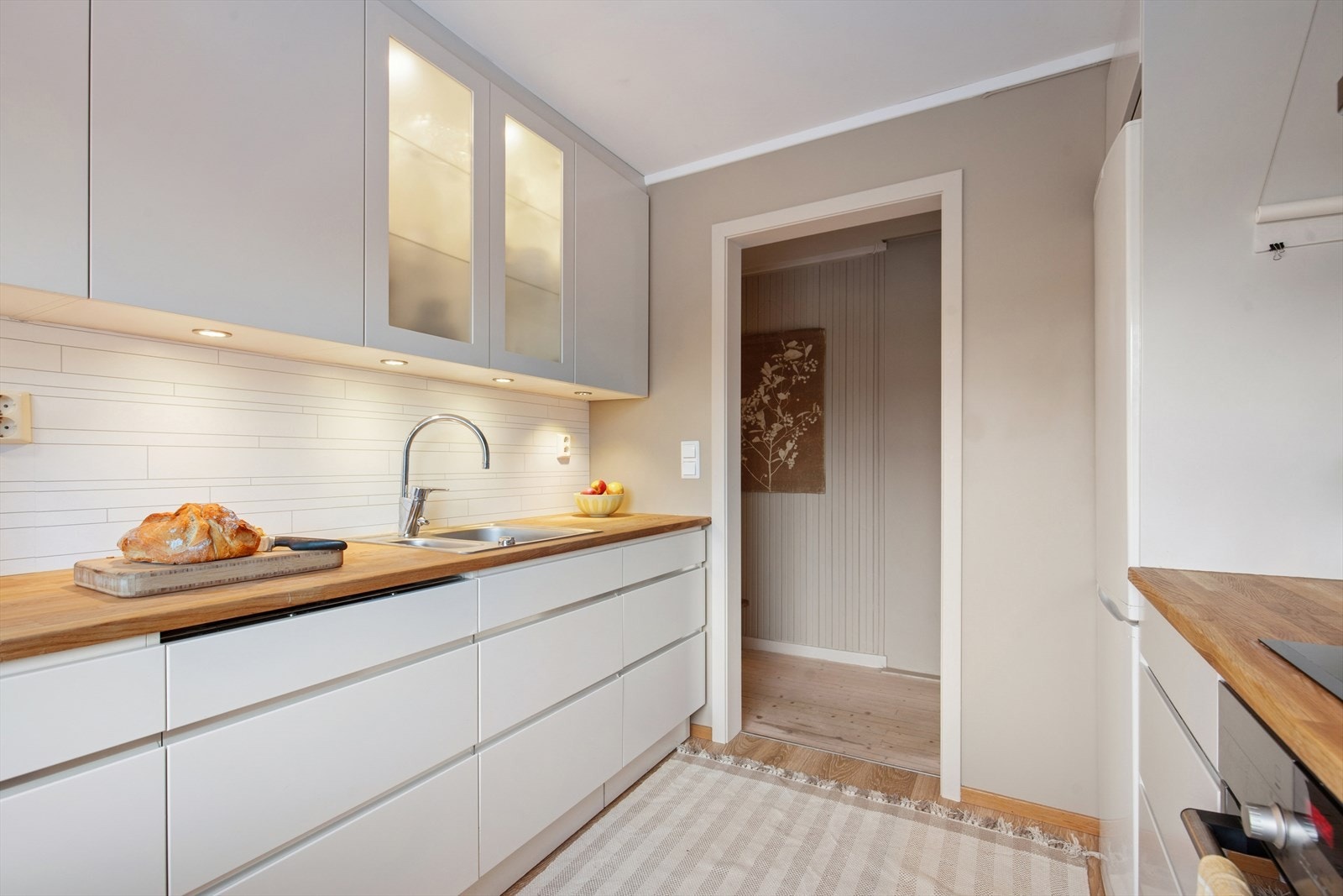 Kjøkkenet fra 2012 har en hvit, glatt innredning med heltre benkeplate og utslagsvask med blandebatteri. Galleribilde