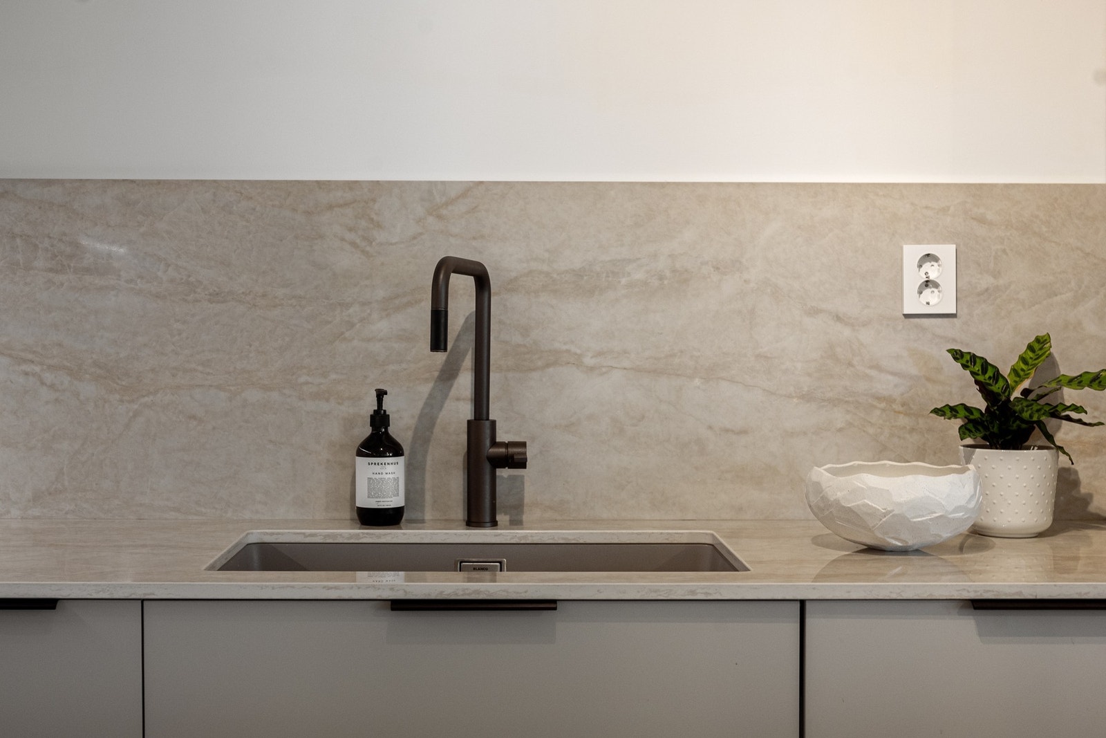 Benkeplate og backsplash fra Dekton i lekker, lys stein (fargen Arga). Tapwell armatur og blanco vask. Galleribilde