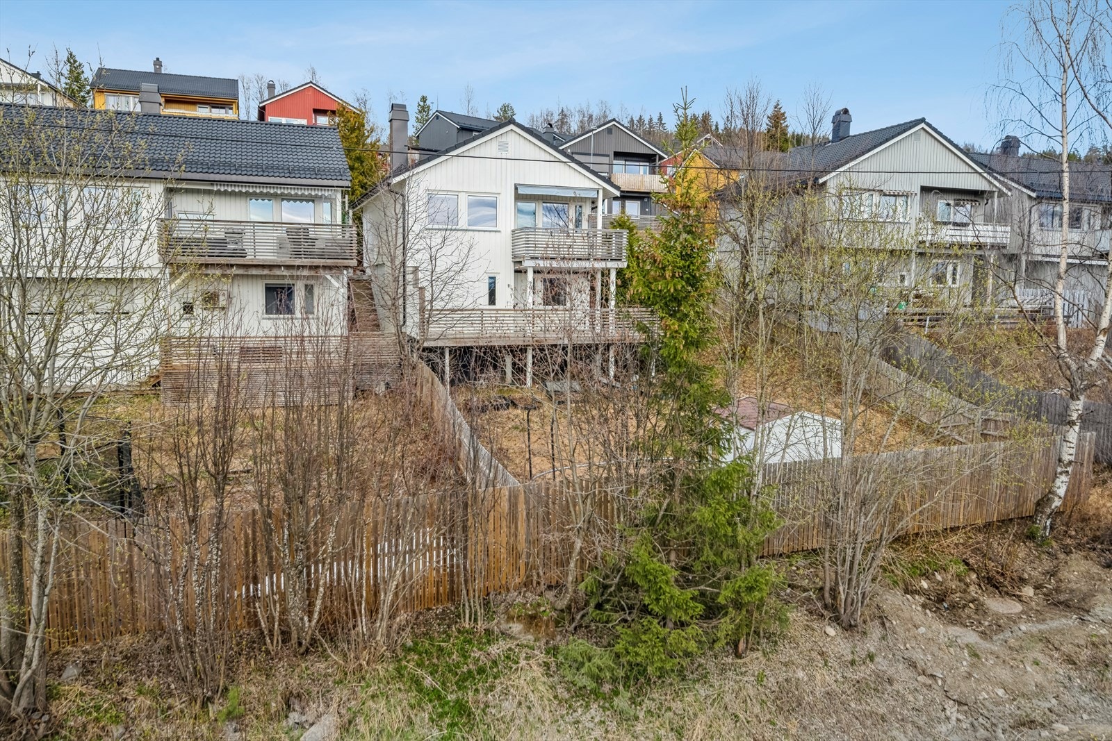 Boligen ligger i skrått terreng med høyt gjerde rundt tomten. Galleribilde