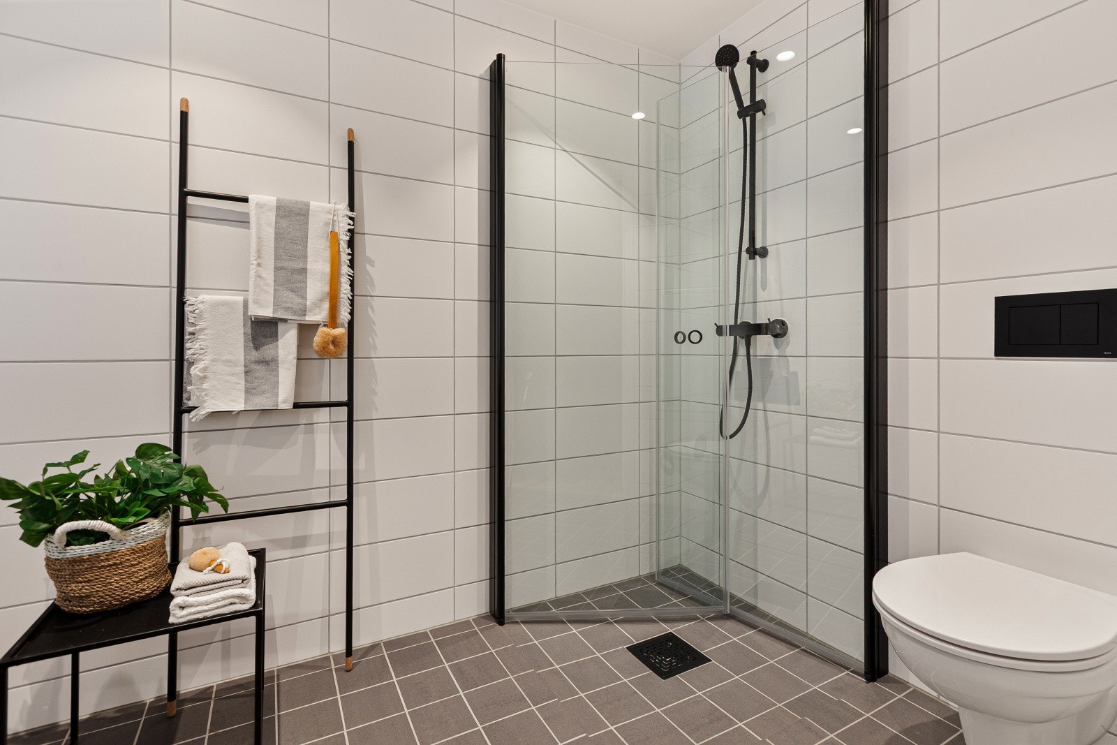 Baderommet har en tidløs baderomsinnredning med skuffeseksjon, speil med tilhørende lys, vegghengt toalett og dusjnisje med innfellbare glassdører. Galleribilde