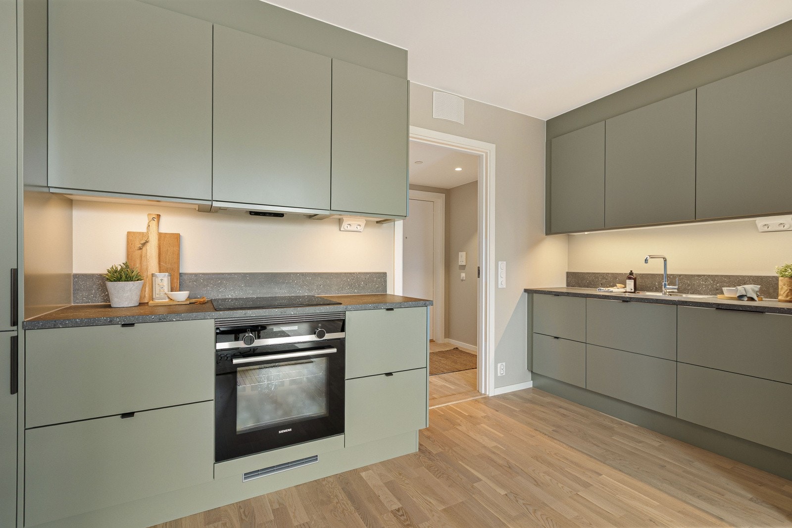 Lengre inn i leiligheten finner vi et stilrent, grønt kjøkken fra Sigdal, som gir en moderne atmosfære. Kjøkkenet har en praktisk laminat benkeplate og behagelig belysning under overskapene, noe som skaper et innbydende arbeidsmiljø for matlagning. Galleribilde