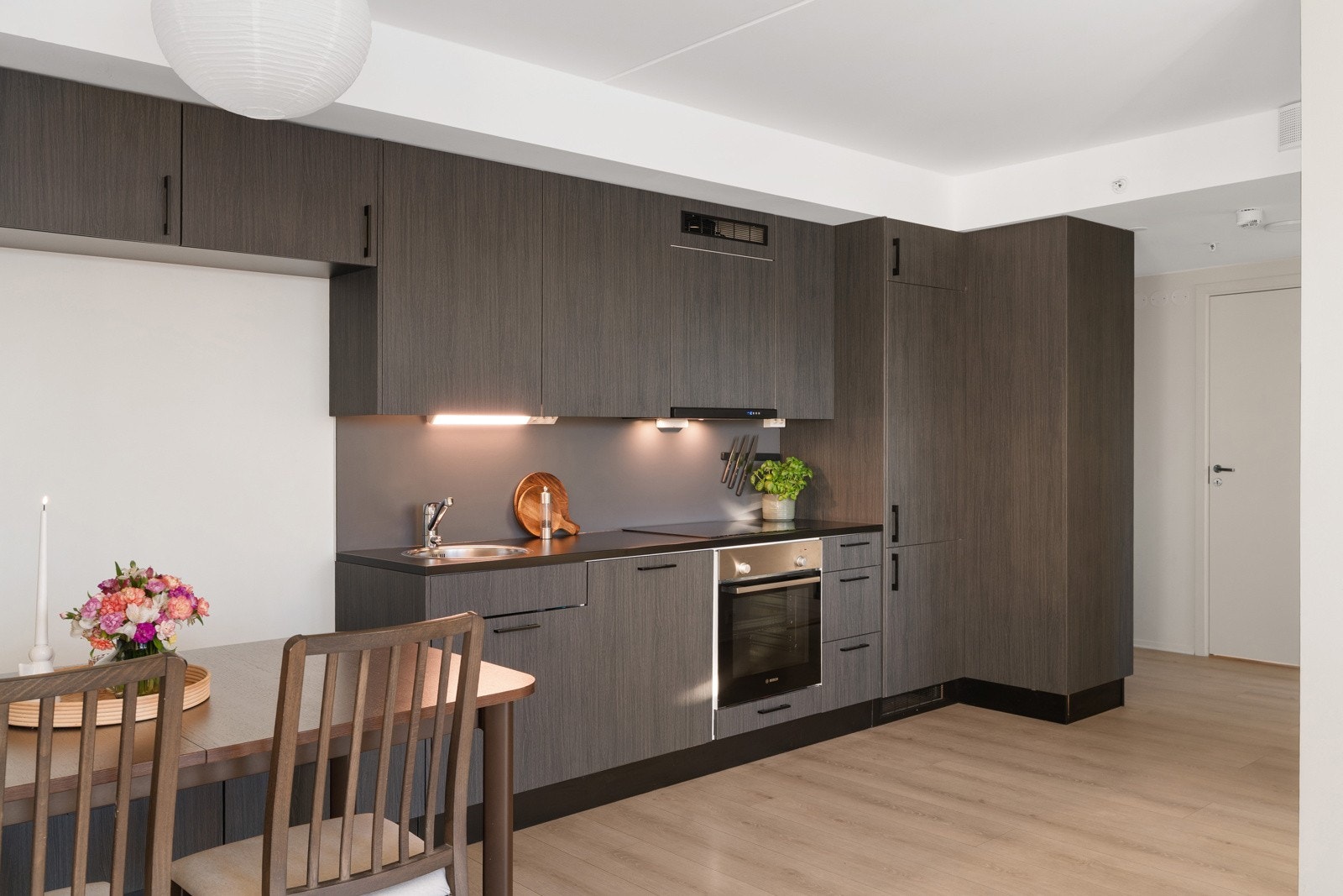 Stilrene materialvalg med mørk kjøkkeninnredning og 1-stavs laminatgulv i en varm fargetone. Galleribilde