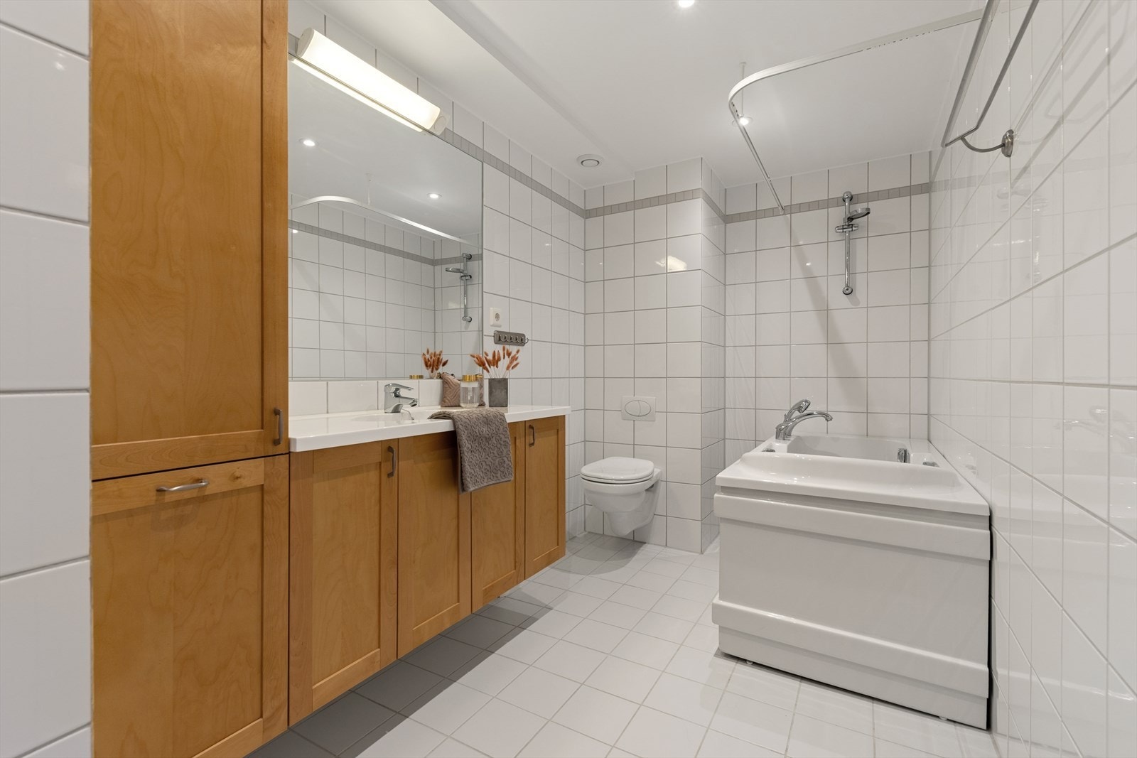 Helfliset baderom med vegghengt toalett, spotter, bred servant med skap, stort speil, og badekar Galleribilde